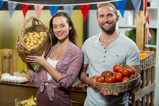 Vendedores de hombre y mujer sosteniendo una canasta de tomates y papas