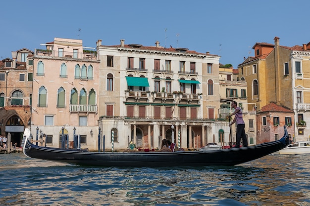 Venedig, Italien - 2. Juli 2018: Nahaufnahme der Gondel mit Menschen und Gondoliere, im Hintergrund die historischen Gebäude des Canal Grande (Canal Grande). Sonniger Sommertag und blauer Himmel