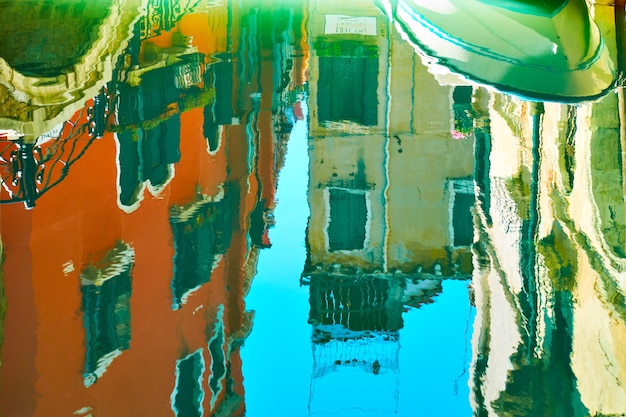 Venezianischer Spiegel - Gebäude, kleine Brücke, Boot und blauer Himmel spiegeln sich in der Wasseroberfläche des Kanals. Venedig in Wasserreflexionen