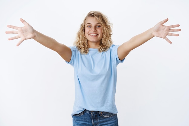 Venha abraço rápido. Retrato de simpática e acolhedora loira carismática charmosa com olhos azuis, braços abertos em abraço, sorrindo amplamente, alcançando a câmera em branco. Copie o espaço