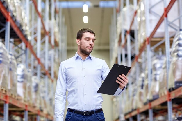 Foto venta al por mayor, logística, negocios, exportación y concepto de personas - hombre o gerente con portapapeles revisando mercancías en el almacén