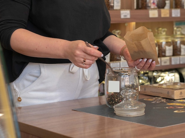 La venta al por menor de té, el vendedor vierte una cuchara de un frasco de una lata en una bolsa