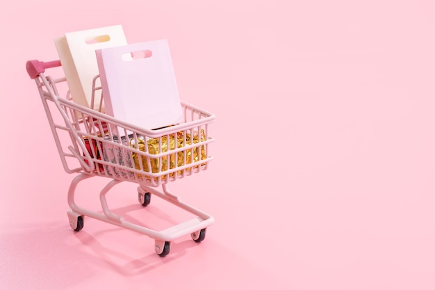 Venta anual temporada de compras concepto mini tienda rosa carro carro lleno de bolsa de papel regalo aislado sobre fondo rosa pálido espacio de copia en blanco cerrar