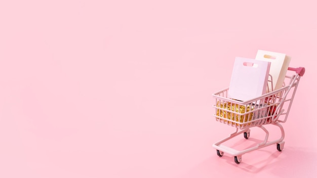 Venta anual temporada de compras concepto mini tienda rosa carro carro lleno de bolsa de papel regalo aislado sobre fondo rosa pálido espacio de copia en blanco cerrar