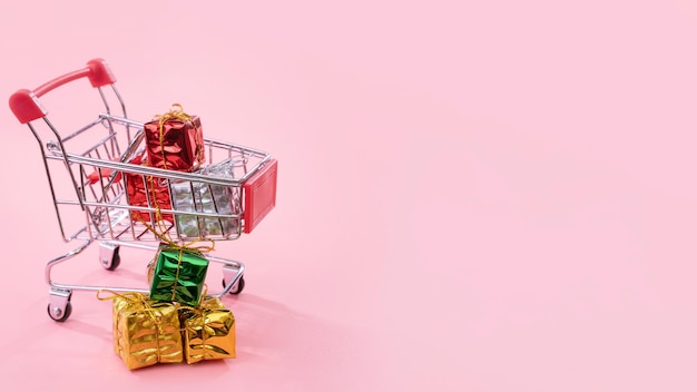 Venta anual temporada de compras navideñas concepto mini carrito de compras rojo lleno de caja de regalo aislado sobre fondo rosa pálido copia espacio cerrar