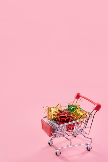 Venta anual temporada de compras navideñas concepto mini carrito de compras rojo lleno de caja de regalo aislado sobre fondo rosa pálido copia espacio cerrar