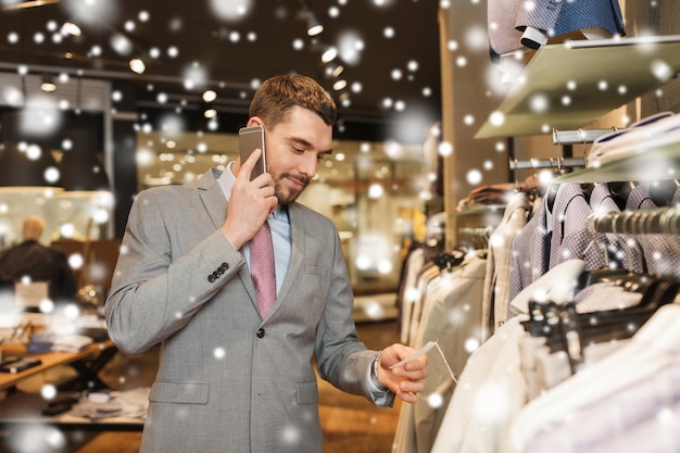 venta, compras, moda, comunicación y concepto de personas - joven feliz o hombre de negocios llamando por teléfono inteligente y eligiendo ropa en la tienda de ropa sobre la nieve