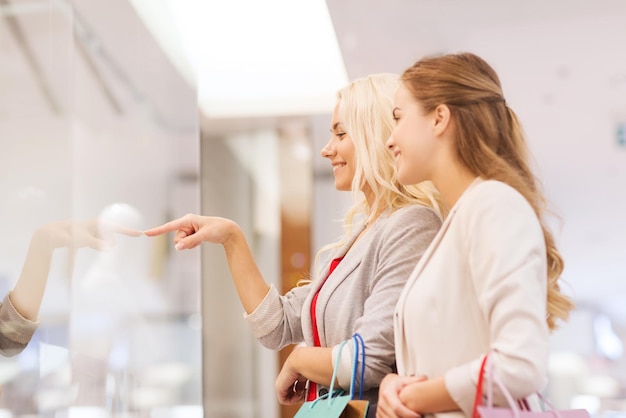 venta, consumismo y concepto de personas - mujeres jóvenes felices con bolsas de compras señalando con el dedo en el centro comercial