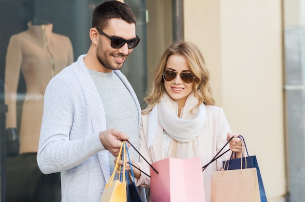 venta, consumismo y concepto de personas - pareja feliz mirando una bolsa de compras en la ventana de la tienda en la calle de la ciudad