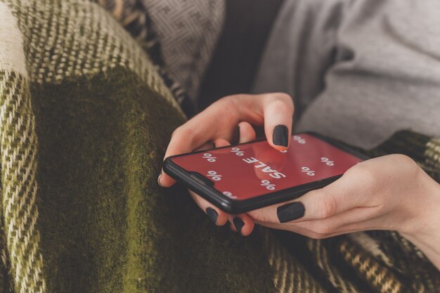 Venta en la pantalla del teléfono. La mujer sostiene un teléfono en su mano y ve la venta de la inscripción. Compras en línea sin salir de casa durante la cuarentena. Venta de viernes negro