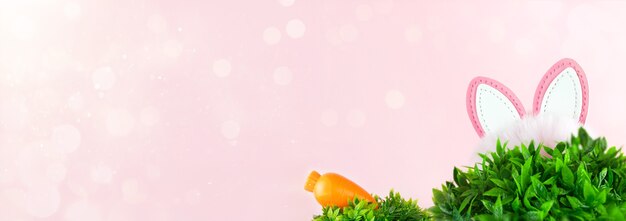 Venta de Pascua con orejas de conejo y zanahoria en pasto sobre fondo rosa.