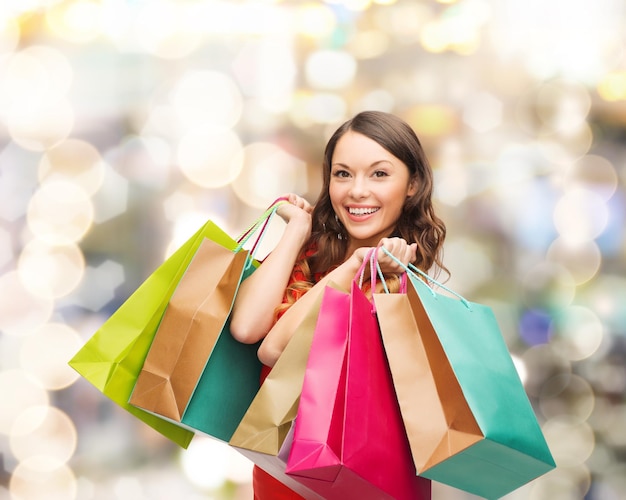 venta, regalos, navidad, vacaciones y concepto de la gente - mujer sonriente con coloridas bolsas de compras sobre fondo de luces
