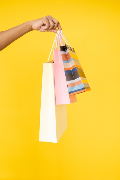 Venta de tienda Comercio minorista Regalos navideños Primer plano de una mano de mujer sosteniendo bolsas de papel de compras aisladas sobre fondo naranja