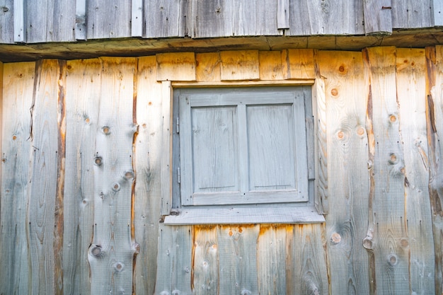 Ventana cerrada muy pequeña en una hermosa pared de madera de una casa antigua con patrones inusuales