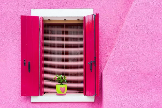 Ventana con contraventanas rosas en la pared rosa. Arquitectura colorida en la isla de Burano, Venecia, Italia.