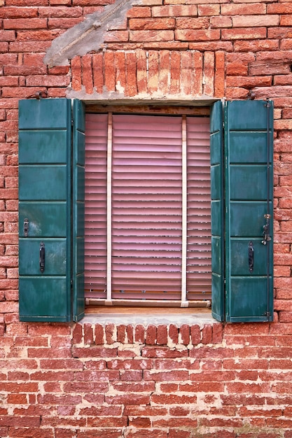 Ventana con contraventanas verdes en la pared de ladrillo rojo de las casas. Italia, Venecia, Burano.