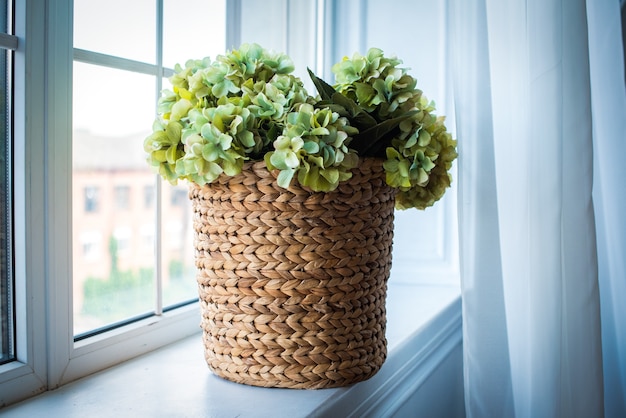 En la ventana hay una canasta de mimbre con hortensias de color verde claro.