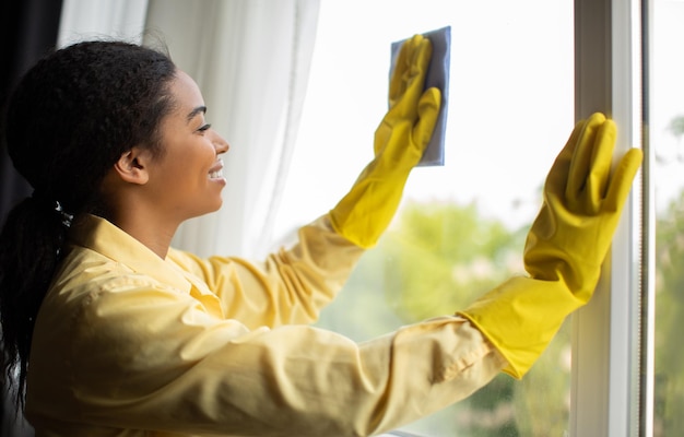 Ventana de limpieza femenina alegre con guantes de trapo en casa