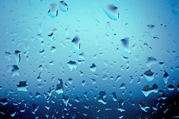 Ventana mojada húmeda con agua corriendo por la superficie Cristal de la ventana después de fuertes lluvias Resumen fondo azul borroso Enfoque suave selectivo