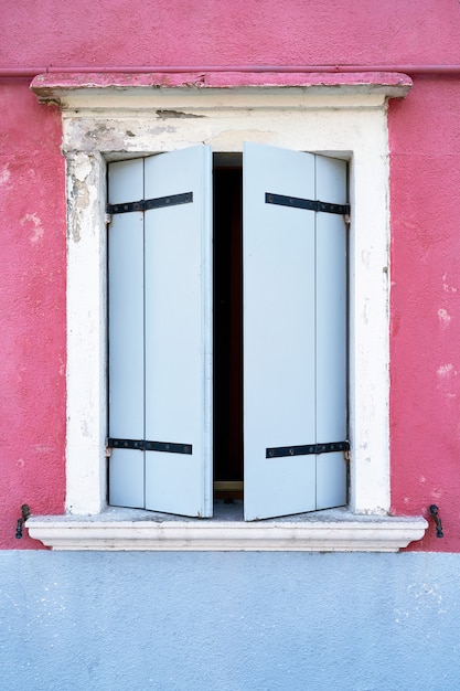 Ventana con persiana azul en la pared de color rosa.