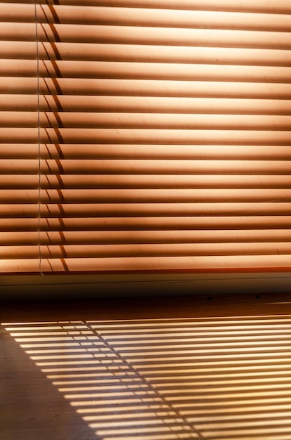 Ventana con persianas horizontales modernas cerradas sombra rayada del sol cae sobre el alféizar de madera