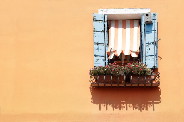 Ventana con persianas de madera azul y toldo a rayas en una pared pintada de naranja