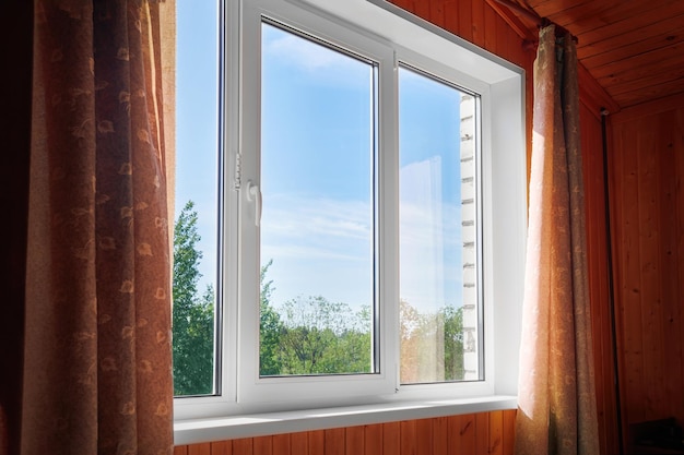 Ventana de plástico cerrada y pared dentro de la habitación Ventana con vista al patio trasero soleado de verano de una casa de campo de madera