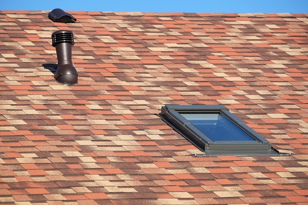 Foto ventana del techo y tubo de ventilación en una casa residencial cubierta de tejas suaves y variopintas de cerca