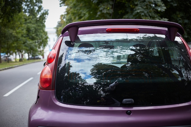 Ventana trasera del coche morado aparcado en la calle en un día soleado de verano, vista trasera. Maqueta para calcomanías o calcomanías