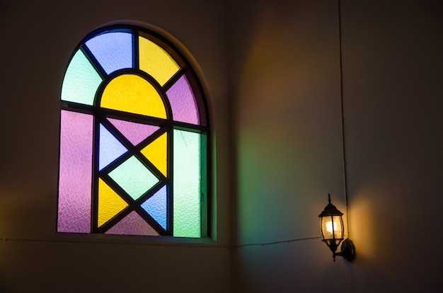 Ventana de vidrio colorido con luz de lámpara en pared