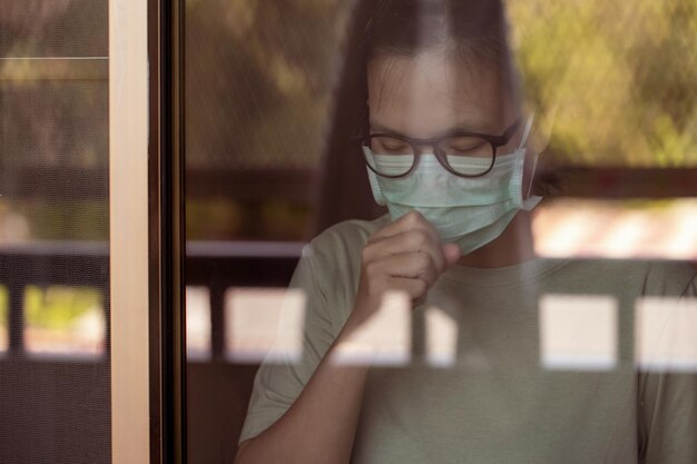 En la ventana de vidrio Una mujer asiática con mascarilla tosiendo debido a problemas respiratorios.