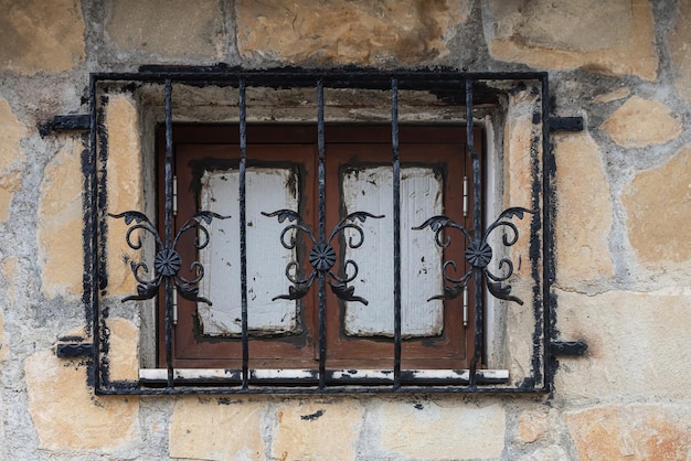 Ventana vintage de madera marrón de primer plano tras las rejas en una antigua casa de piedra