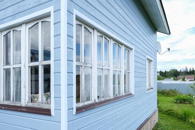 Ventanas blancas de una pequeña casa de estructura diminuta con paredes azules, una residencia de campo en un día soleado de verano.