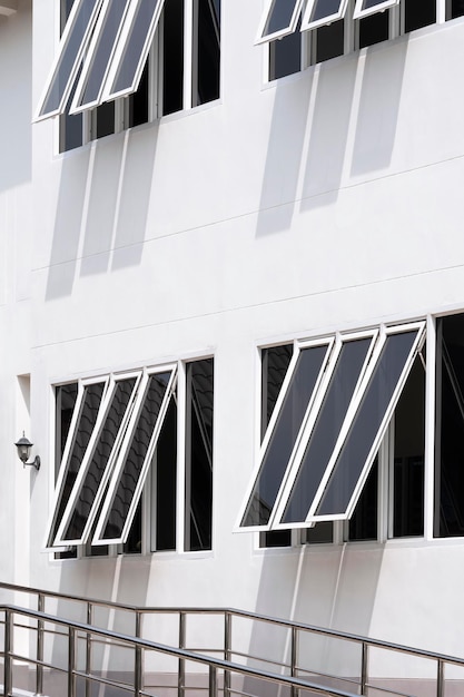 Ventanas de vidrio en una pared de cemento blanco con barandilla de acero inoxidable en la acera fuera de un edificio moderno