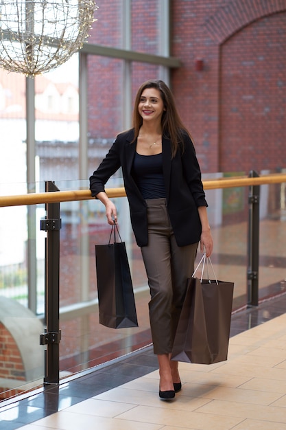 Ventas. Compras. Chica atractiva con ropa elegante con grandes bolsas de compras en el centro comercial.