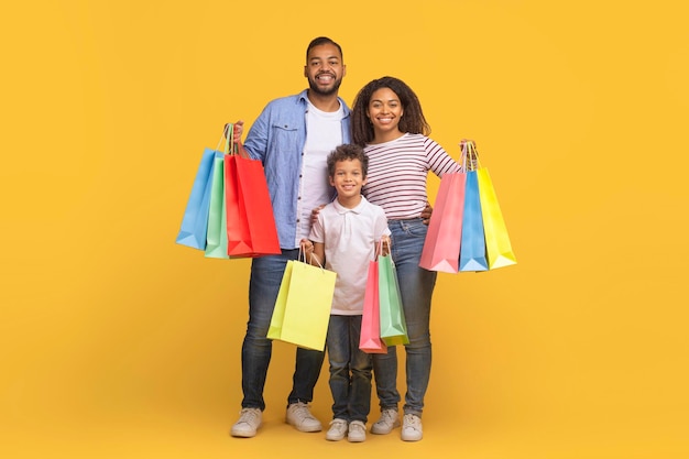 Ventas estacionales familia negra feliz con un hijo pequeño sosteniendo bolsas de compras