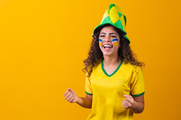 Ventilador brasileño. usando pintura como maquillaje, fan brasileño celebrando el fútbol o el partido de fútbol sobre fondo amarillo. Colores de Brasil.