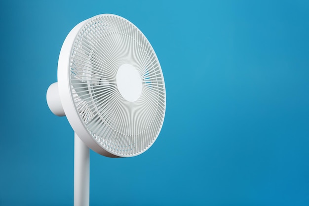 Ventilador elétrico moderno branco para resfriar a sala sobre um fundo azul.