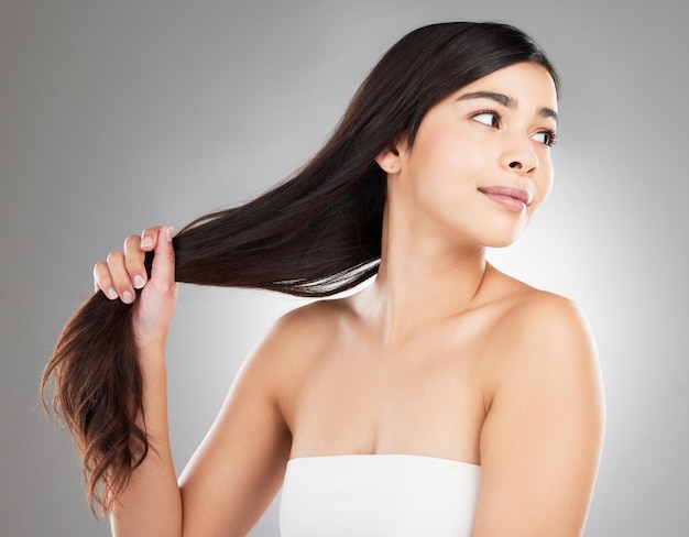 Veo una tijera afilada como una amenaza. Foto de estudio de una hermosa joven mostrando su largo cabello sedoso contra un fondo gris.