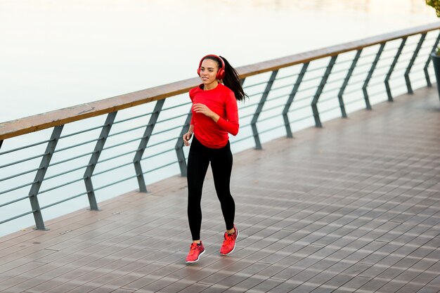 Ver en activo bella mujer joven corriendo en el paseo junto al río