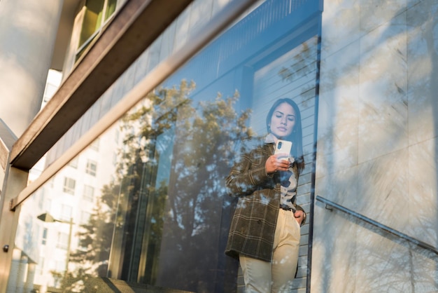 Ver através do uso de mulher de negócios de vidro de telefone inteligente na cidade vestindo camisa e jaqueta formal