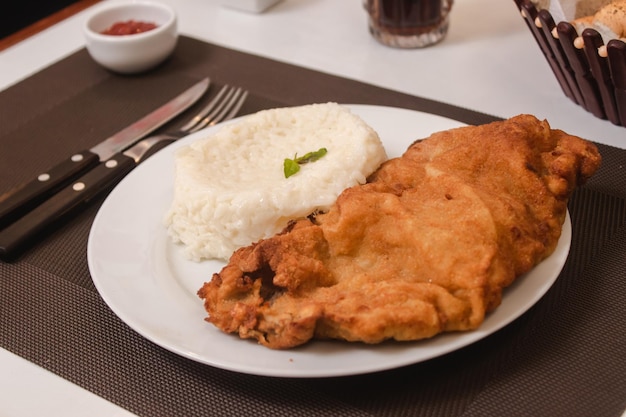 Ver detalle de arroz con milanesa servido en un plato con soda y pan