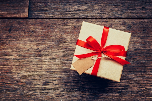 Ver por encima de la caja de regalo marrón y cinta roja con etiqueta sobre fondo de madera con espacio.