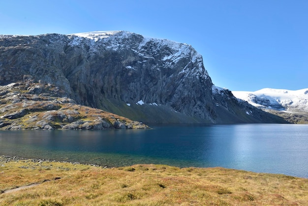 Ver en un lago bordeado por montañas nevadas y hierba amarilla en Noruega