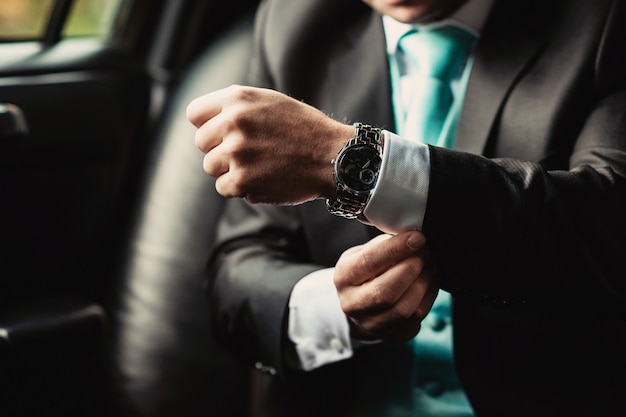 Ver en la mano del hombre elegante en un traje de negocios sentado en el auto