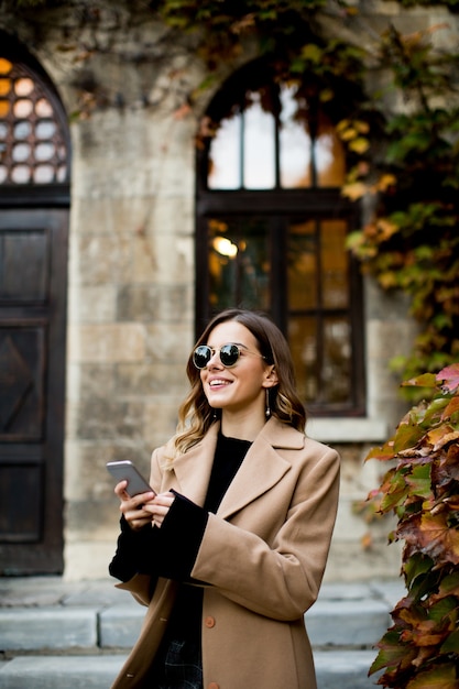 Ver en la mujer moderna con teléfono móvil en otoño al aire libre