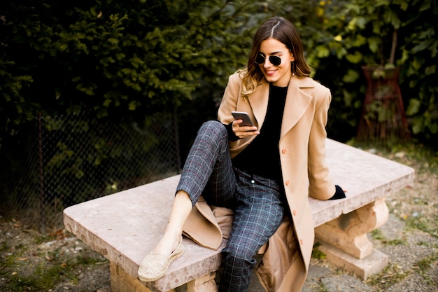 Ver en la mujer moderna con teléfono móvil en otoño al aire libre