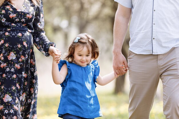 Ver en niño pequeño. La madre, el padre se toman de la mano, la hija disfruta de la naturaleza y camina en el parque de la primavera.