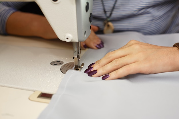 Ver os de cima nas mãos do alfaiate feminino trabalhando na máquina de costura. indústria de fabricação de roupas