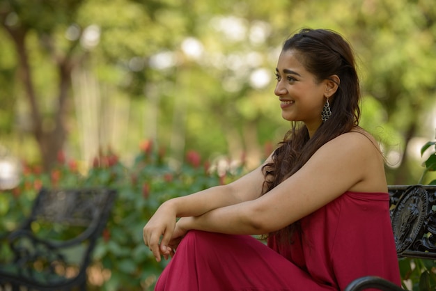 Ver perfil de feliz joven hermosa mujer india sentada en el parque